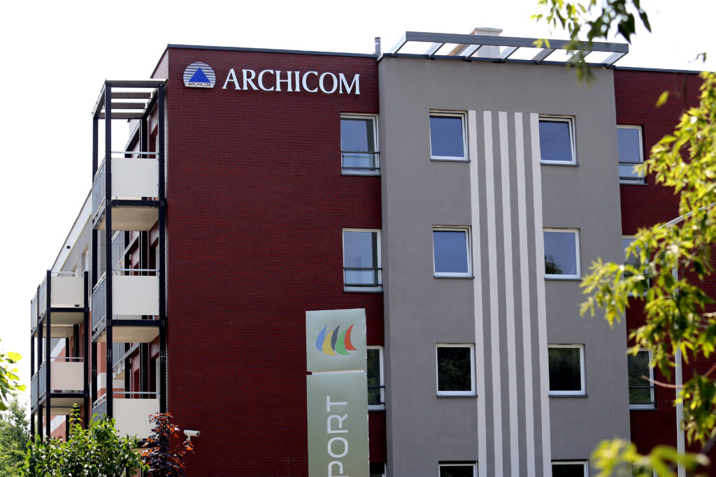 Blok z fasadą z czerwonej cegły, na szczycie elewacji napis Archicom wraz z logo dewelopera
