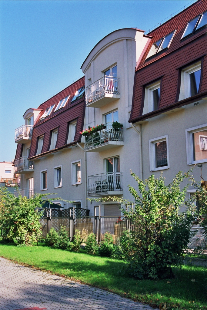 Ujęcie na elewację budynku i balkony schowane za zielenią
