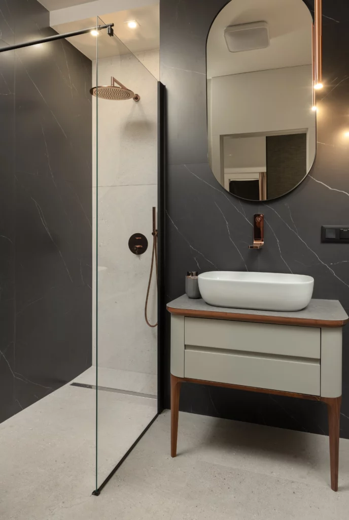 Miedziane elementy w łazience spajają matowe, kontrastujące czarne i off white’owe płytki.