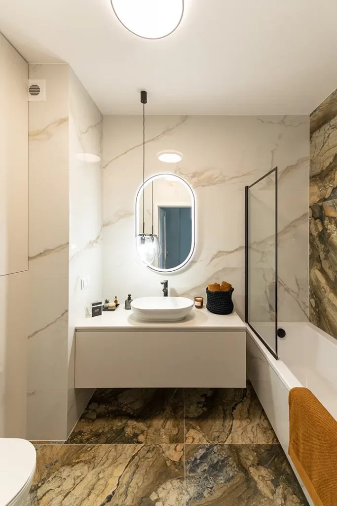Druga łazienka to coś dla miłośników kąpieli w wannie. Aby projekt był spójny użyto tych samych płytek, jednak w tym wypadku na podłodze znalazł się hipnotyzujący gres imitujący kamień naturalny, a białe marmury dopełniają aranżację tylko na ścianach.