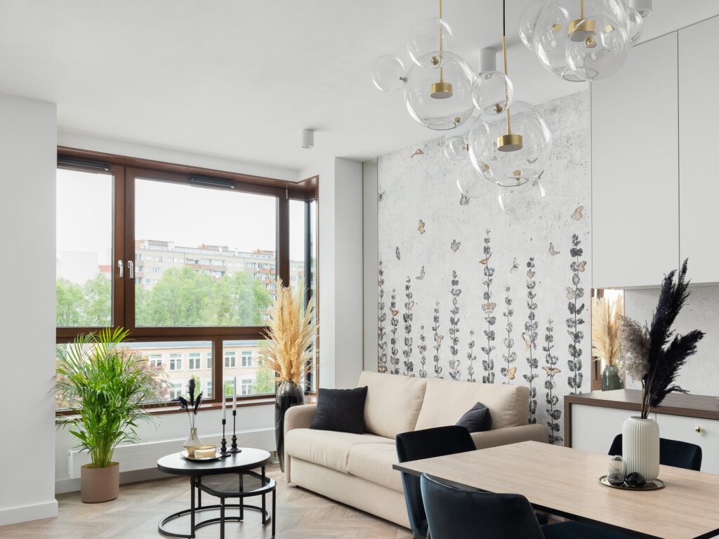 Przytulny salon jest wzbogacony żyrandolami inspirowanymi mydlanymi bańkami, które tematycznie nawiązują do beztroskiego spokoju wiosny. Pastelowe kolory: beże, jasne szarości wzmocnione czernią spajają wnętrze całego apartamentu.